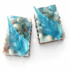 Two pieces of soap with blue leaf designs and seashell textures on a white background